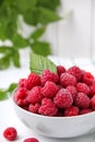 Bowl of fresh ripe raspberries with green leaf on white table against blurred background, closeup Royalty Free Stock Photo