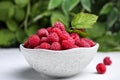 Bowl of fresh ripe raspberries with green leaves on white table against blurred background, closeup Royalty Free Stock Photo