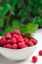 Bowl of fresh ripe raspberries with green leaves on white table against blurred background. Space for text Royalty Free Stock Photo