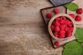 Bowl with fresh ripe raspberries and green leaves on wooden table, flat lay. Space for text Royalty Free Stock Photo