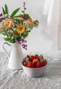 A bowl of fresh strawberries and a bouquet of autumn flowers on the table in a bright room Royalty Free Stock Photo