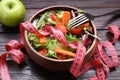 Bowl with fresh vegetable salad, fork, apple and measuring tape on wooden table, closeup. Healthy diet concept Royalty Free Stock Photo