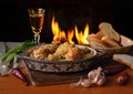 A bowl of fried chicken legs, bread, pepper, garlic on a wooden table and fire in the background. Royalty Free Stock Photo