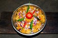 Bowl of fried noodles recipe with onion slices, red tomato, red and green pepper and vegetables on wooden background top view in Royalty Free Stock Photo