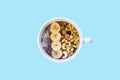 Bowl of fruit smoothie with nuts and banana, top view. Flat lay of an acai bowl with cereals, cashews and hazelnuts in blue bright