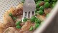 A fork stuck in a bowl full of cottage pie and peas