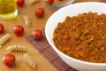 Bowl full of italian classic ragu bolognese sauce on the table with some pasta, tomatoes and a glass of olive oil