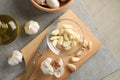 Bowl of garlic slices, bulbs, oil, knife, board on grey wooden background