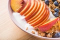 Bowl of granola with yogurt, peach slices and bluberry on a wooden table