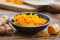 A bowl of grated fresh turmeric roots. Whole curcuma roots, cutting board and grater on background.