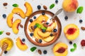 Bowl of greek yogurt with peach, oats, nuts, mint, honey and blueberries with a spoon for healthy breakfast