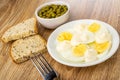 Bowl with green peas, slices og bread, fork, pieces of egg with mayonnaise in saucer on wooden table