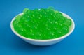 Bowl of Green Popping Boba Pearls on a Bright Blue Background