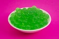 Bowl of Green Popping Boba Pearls on a Bright Pink Background