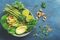 A bowl of green vegan salad with asparagus, avocado, lettuce, basil, mint, microgreen, lime and cashew nuts, blue rustic