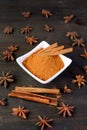 Bowl of ground cinnamon powder and sticks with star anise scattered on black wooden table Royalty Free Stock Photo