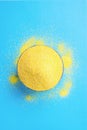 Bowl with Heap of Dry Uncooked Vibrant Yellow Color Polenta Spilled on Light Blue Background. Top View. Creative Image.