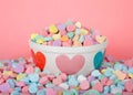 Valentine candy hearts in and around holiday bowl pink background