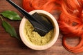 Bowl of henna powder, brush, green leaves and red strand on wooden table, flat lay. Natural hair coloring Royalty Free Stock Photo