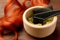 Bowl of henna powder, brush and red strand on wooden table, closeup. Natural hair coloring Royalty Free Stock Photo