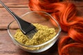 Bowl of henna powder, brush and red strand on wooden table, closeup. Natural hair coloring Royalty Free Stock Photo