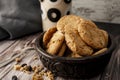 Bowl with homemade oatmeal cookies with raisins and seeds, raisins and cereal dumped on the table and a glass of milk behind.