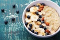 Bowl of homemade oatmeal porridge with banana, blueberries, almonds, coconut and caramel sauce on teal rustic table from above