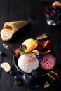 Bowl with ice cream with three different scoops of white, yellow, red colors and waffle cone, chocolate, tangerines and Royalty Free Stock Photo