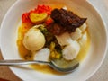 A bowl of Indonesian food contains potato, beef, soup, rice cake & x28;lontong& x29;, egg, broccoli and chili sauce.