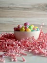 Bowl of jelly beans pastel colored on a bed of shredded pink paper crinkled up with a wooden background for Easter