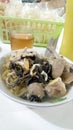 A bowl of meatballs with pieces of beef skin accompanied by a glass of hot tea.