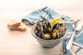 Bowl with mussels, lemon and herbs, a blue towel, spoon and bread on a light wooden table, copy space