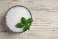 Bowl of natural sea salt and basil leaf on white wooden table, top view. Space for text Royalty Free Stock Photo