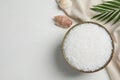 Bowl of natural sea salt, shell and leaf on white wooden table, flat lay. Space for text