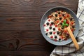 Bowl with oat granola, yogurt and black raspberries, black and red currants on a brown wooden background. Royalty Free Stock Photo