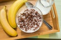 Bowl of oatmeal chocolate flakes in the shape of letters of the alphabet with milk on a wooden tray with bananas and a jug of milk Royalty Free Stock Photo