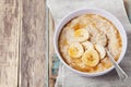 Bowl of oatmeal porridge with banana and caramel sauce on rustic table, hot and healthy breakfast Royalty Free Stock Photo