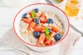 Bowl of oatmeal porridge with blueberries, strawberries, almond petals and honey on a white wooden background. Royalty Free Stock Photo