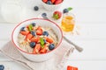 Bowl of oatmeal porridge with blueberries, strawberries, almond petals and honey on a white wooden background. Royalty Free Stock Photo