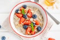 Bowl of oatmeal porridge with blueberries, strawberries, almond petals and honey on a white wooden background. Royalty Free Stock Photo