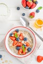 Bowl of oatmeal porridge with blueberries, strawberries, almond petals and honey on a white wooden background. Royalty Free Stock Photo