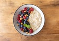 Bowl of oatmeal porridge with various berry and nuts on wooden table top view. Healthy and diet breakfast