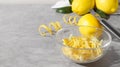 Bowl with peel pieces, fresh lemons and zester on grey table, space for text