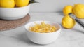 Bowl with peel pieces, fresh lemons and zester on white marble table