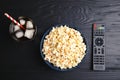 Bowl with popcorn, glass of iced cola and TV remote on wooden background, top view