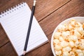 A bowl of popcorn and notebook and Black pencil on a wooden table. Royalty Free Stock Photo