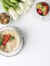 Bowl with porridge, banana, strawberries, white tulips on white table. Copy space