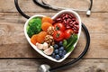 Bowl with products for heart-healthy diet and stethoscope on wooden background Royalty Free Stock Photo
