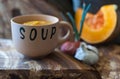 Bowl of pumpkin soup on wooden surface with onion and pumpkin blur background