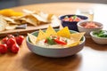 bowl of queso dip surrounded by tortilla chips on a wooden table Royalty Free Stock Photo